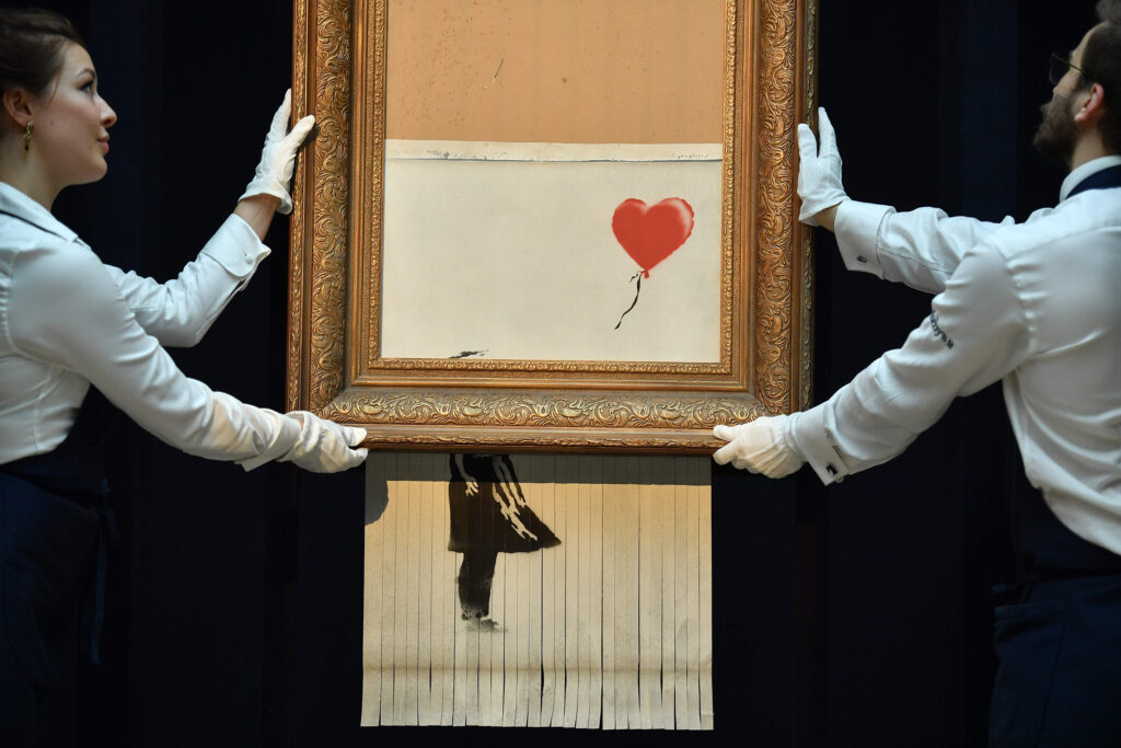 Empleados de Sotheby's sosteniendo la pieza "Love is in the Air" (2018) de Bansky, que surgió a partir de la autodestrucción de la obra "Girl With a Balloon" (2006) del mismo artista.