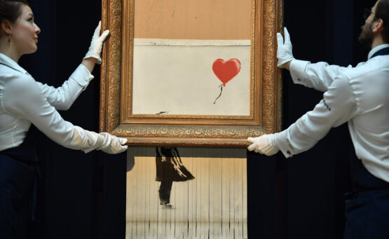 Empleados de Sotheby's sosteniendo la pieza "Love is in the Air" (2018) de Bansky, que surgió a partir de la autodestrucción de la obra "Girl With a Balloon" (2006) del mismo artista.
